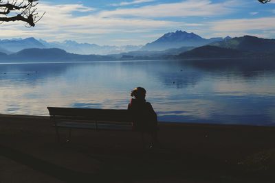 Woman sitting on seat by lake against sky in switzerland 