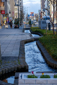 People on footpath by canal in city