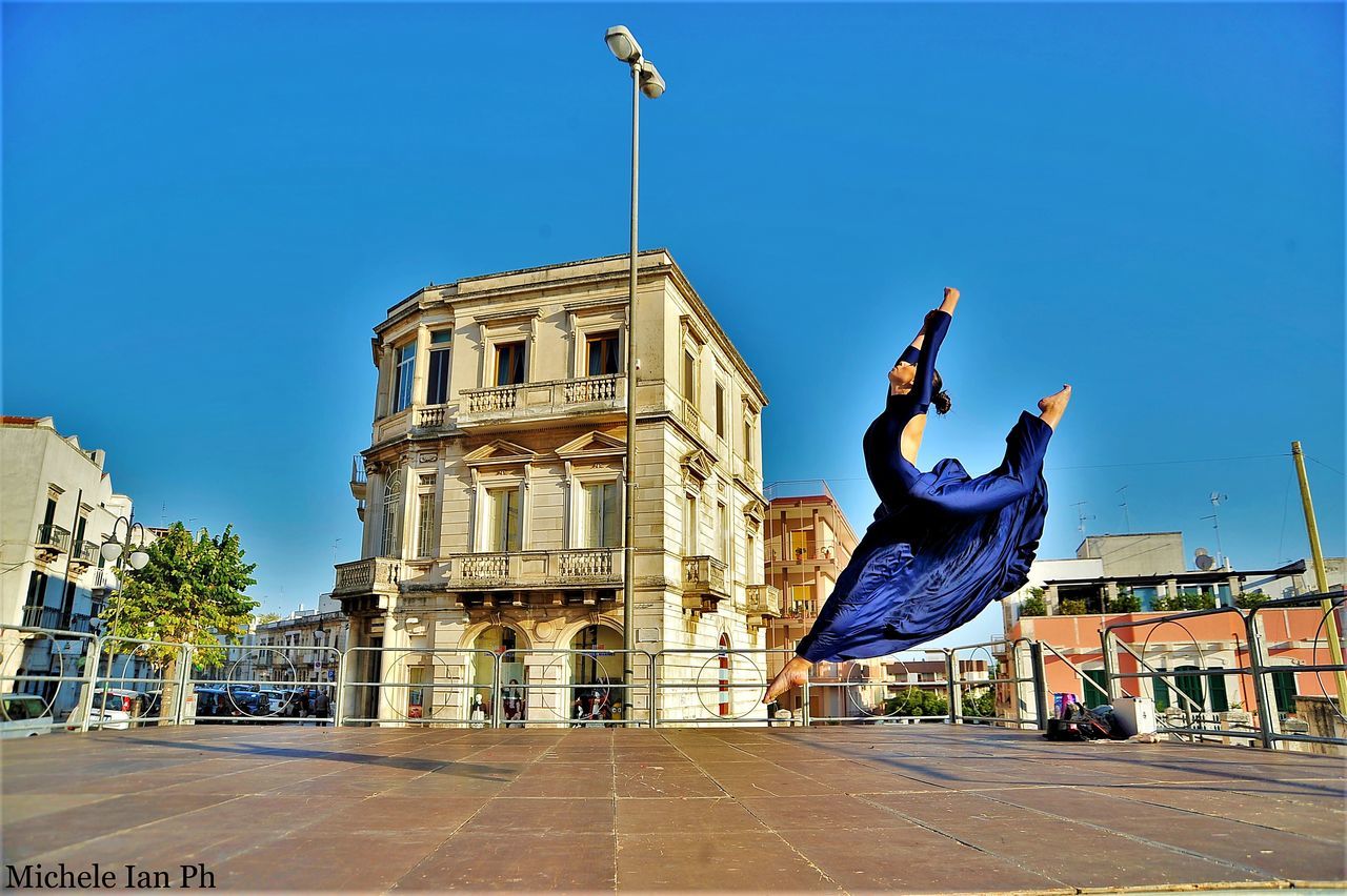 blue, architecture, building exterior, real people, outdoors, built structure, clear sky, day, handstand, men, sky, flexibility, one person, people