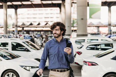 Happy businessman standing in front of cars on road