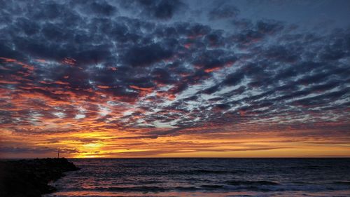 Scenic view of sea against dramatic sky during sunset