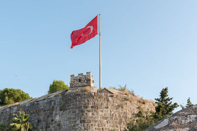 Low angle view of flag against built structure against clear blue sky