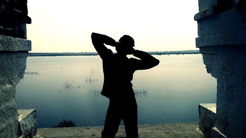 Silhouette couple standing on shore against sky