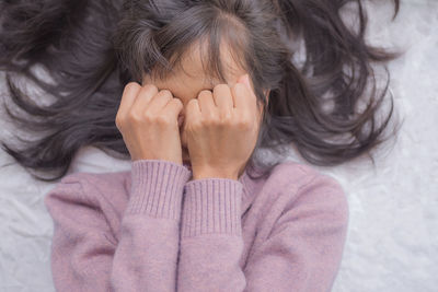 Close-up of girl covering face lying on bed