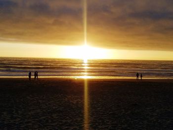 Silhouette people on beach against sky during sunset