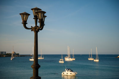 Lamp post at harbor with sea in background against sky during sunset