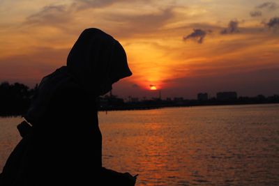 Silhouette woman standing by sea against sky during sunset