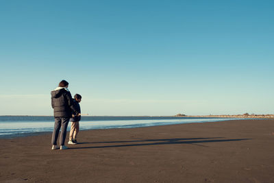 Rear view of man standing at beach against clear sky