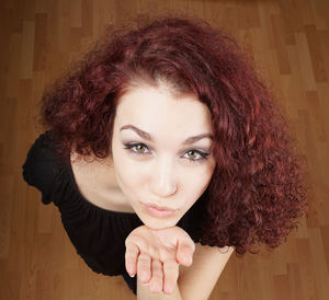 Portrait of beautiful young woman blowing kiss on hardwood floor at home