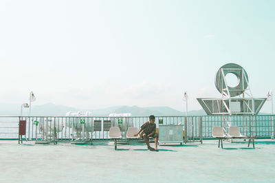 Man sitting on chair at beach against clear sky
