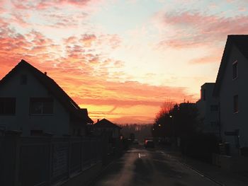 Road amidst houses against sky during sunset