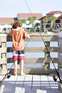 Rear view of boy standing by railing against sky