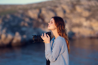 Side view of young woman using phone while standing outdoors