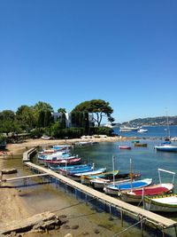 Boats moored at beach against clear blue sky