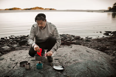 Full length of mature man cooking food on camping stove at lakeshore