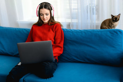 Young woman using laptop while sitting on sofa at home