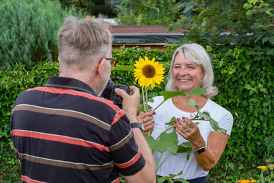 Rear view of people holding flowers against plants