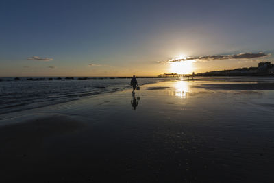 Silhouette man on beach against sky during sunset