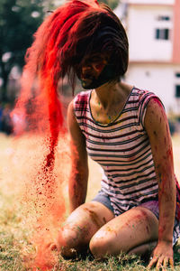 Woman splashing powder paint with hair while sitting on field