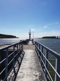 Man standing on railing by sea against clear blue sky