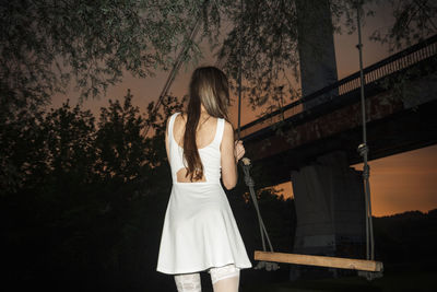 Rear view of woman standing against trees at night