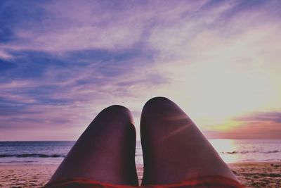 Low section of woman on beach against sky during sunset