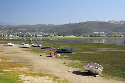 Boats moored on shore by lake against sky