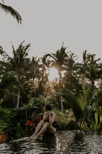Side view of woman sitting on beach against sky