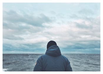 Rear view of man standing at beach against cloudy sky