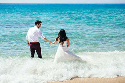 Rear view of newlywed couple walking in sea