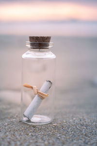 Close-up of a small glass bottle containing a paper message on the beach during sunrise