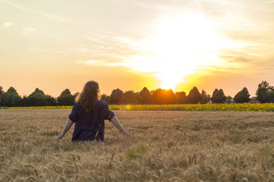 Woman standing on agricultural field against sky during sunset