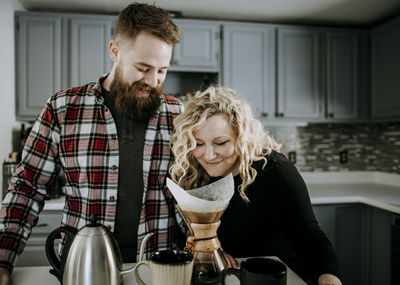 Young female smells morning coffee while husband with beard looks on