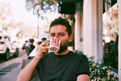 Portrait of young man holding ice cream in city