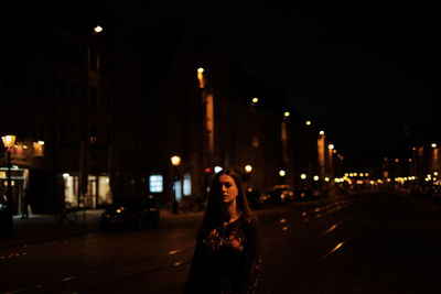 Portrait of woman standing on illuminated street at night