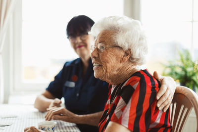 Side view of happy senior woman sitting with caretaker at home