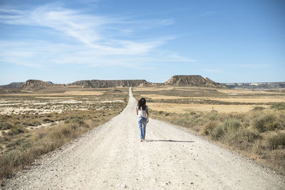 Rear view of mature woman walking on road against sky during sunny day