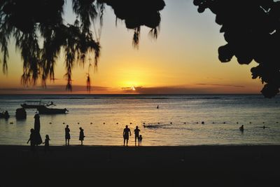 Silhouette people standing on beach against sky during sunset