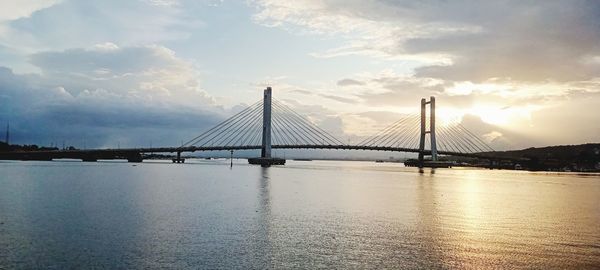 Suspension bridge over river against sky at sunset