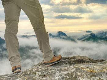 Hiker legs in light outdoor trousers and comfortable leather trekking boot on peak. hiking in nature