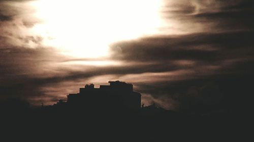 High section of silhouette buildings against clouds