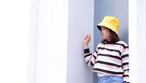 Young woman looking away while standing against wall