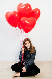 Full length of woman holding heart shaped balloons against wall