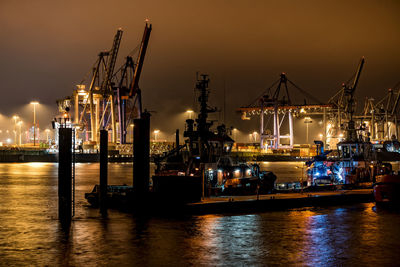 Illuminated commercial dock by sea against sky at night