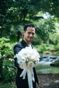 Portrait of smiling young man standing against plants