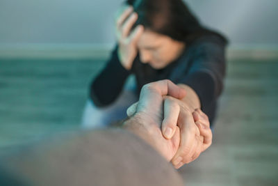 Unrecognizable woman with mental health problems receiving help from man holding her hand