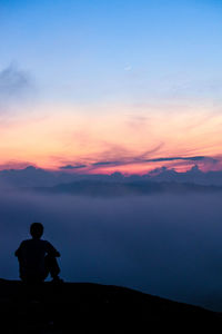 Silhouette man sitting against sky during sunset