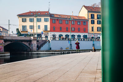 People on bridge over river in city against sky