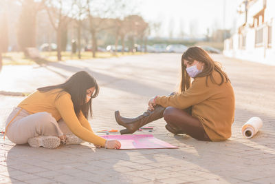Females wearing mask writing on banner while sitting on street