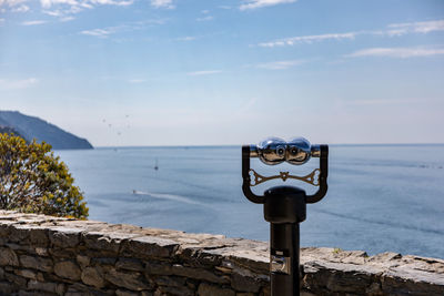 Close-up of coin-operated binoculars by sea against sky
